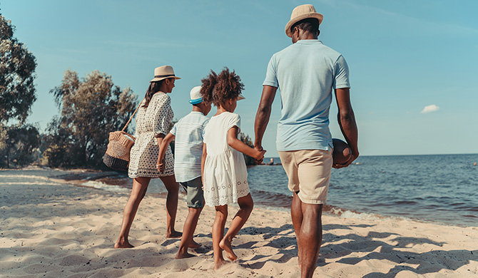Vacances en famille : parents et leurs deux enfant marchent sur la plage