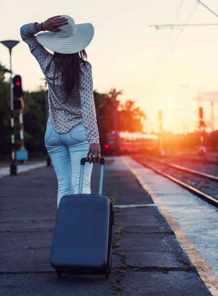 femme sur un quai de gare avec sa valise au coucher du soleil