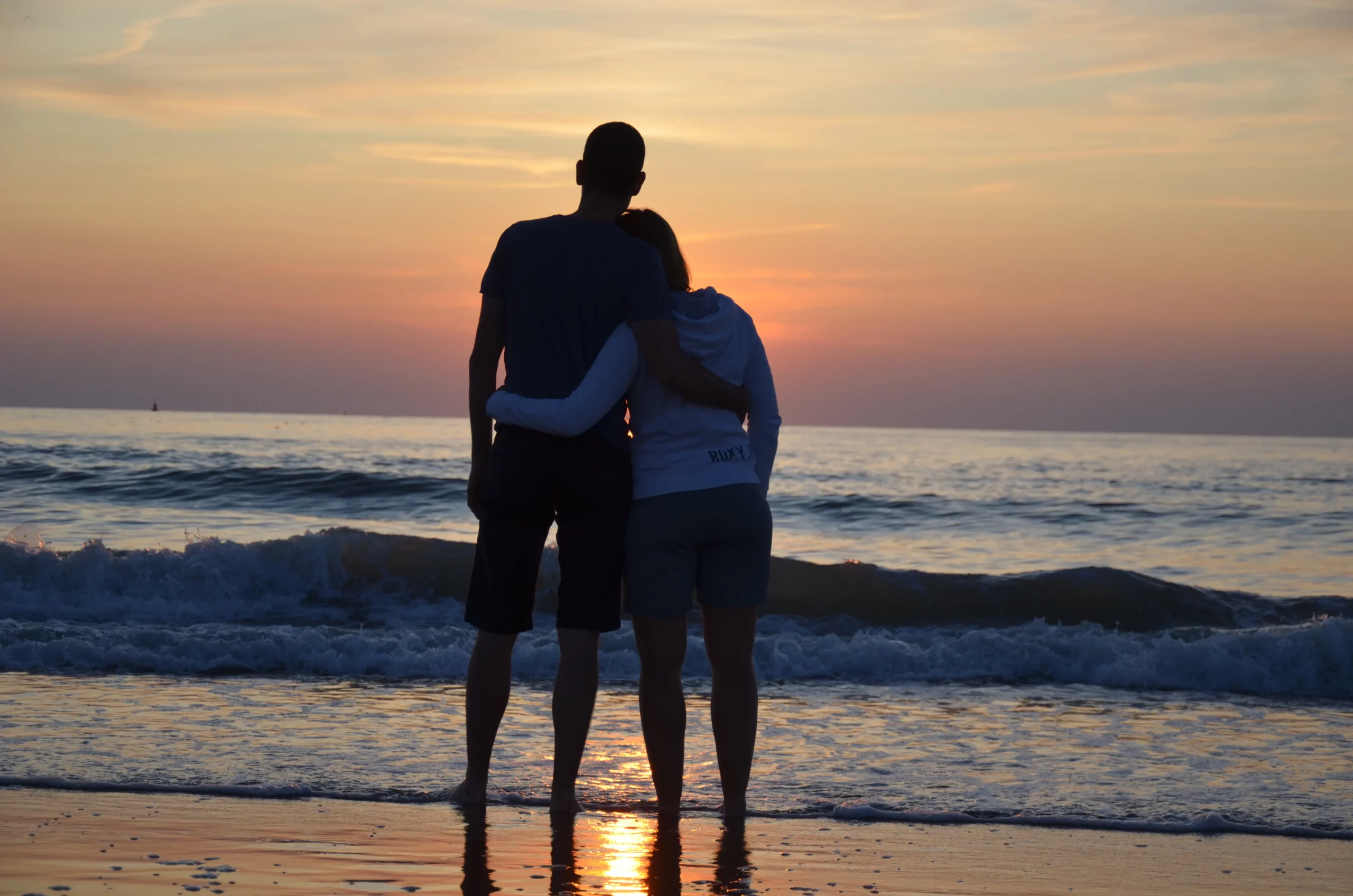 Couple amoureux regardant le coucher de soleil sur la mer, créant un moment romantique.