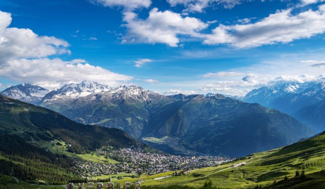 Scenery view of Verbier village surrounded with beautiful Swiss Alps mountains in sunny summer day with green meadows, forests, blue sky.