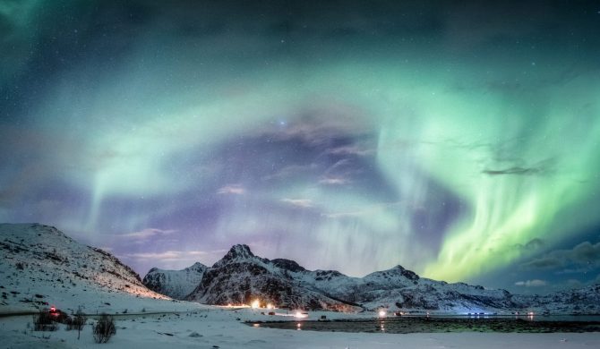 Northern lights explosion on snowy mountain range near coastline at Lofoten islands, Norway