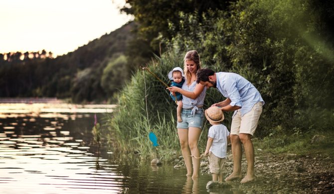 A young family with two toddler children spending time outdoors by the river in summer.