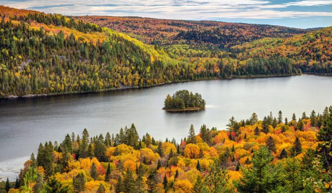 Pine Island in the middle of Wapizagonke lake surrounded by colorful forested hills in Autumn, La Mauricie National Park, Quebec, Canada