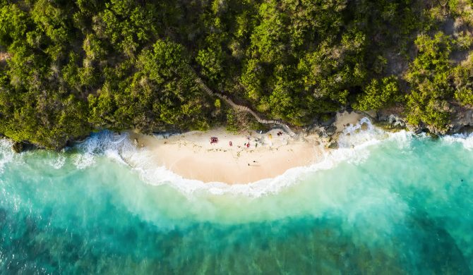 View from above, stunning aerial view of some tourists sunbathing on a beautiful beach bathed by a turquoise rough sea during sunset, Topan Beach, South Bali, Indonesia.