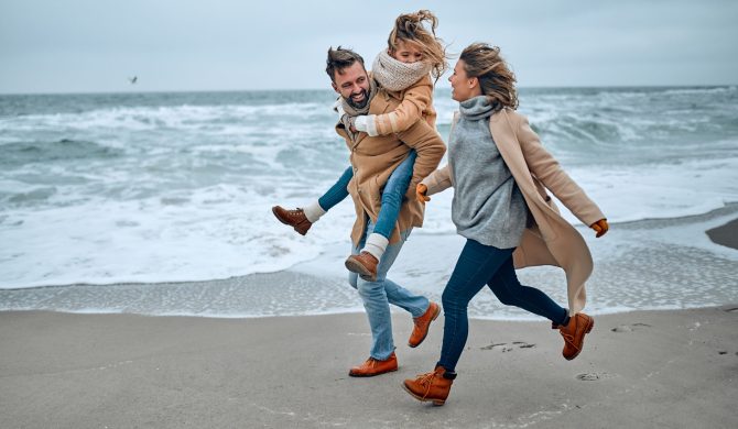 Portrait of a young married couple and their cute daughter who have fun on the beach in winter.