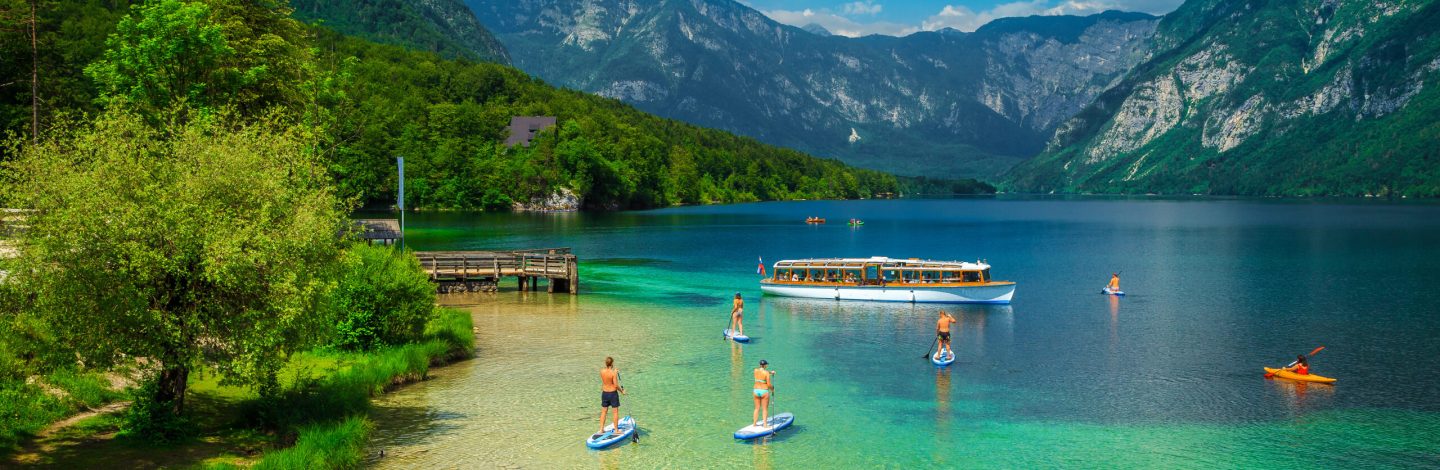 Healthy sporty friends exercising on the colorful sup boards. Active men friends kayaking on the lake Bohinj, Ribcev Laz, Slovenia, Europe