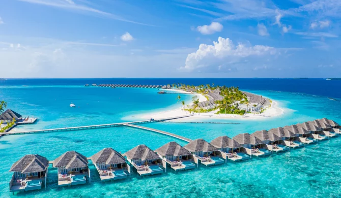 Plage de sable blanc aux Maldives avec une eau turquoise et des palmiers sous un ciel bleu