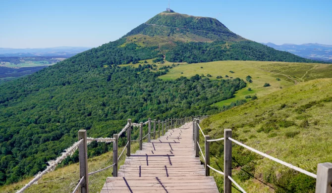 Panorama du Massif Central avec les volcans d'Auvergne et des randonneurs traversant les crêtes verdoyantes.