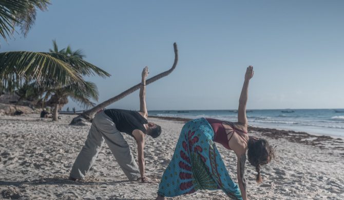 Couple doing yoga at the beach in a sunny day