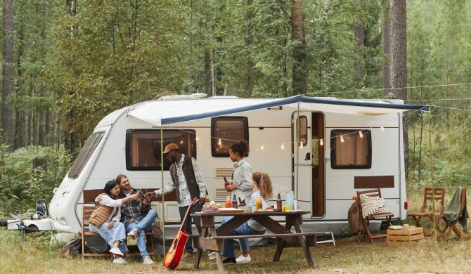 Wide angle view of young people enjoying outdoors while camping with van in forest, copy space