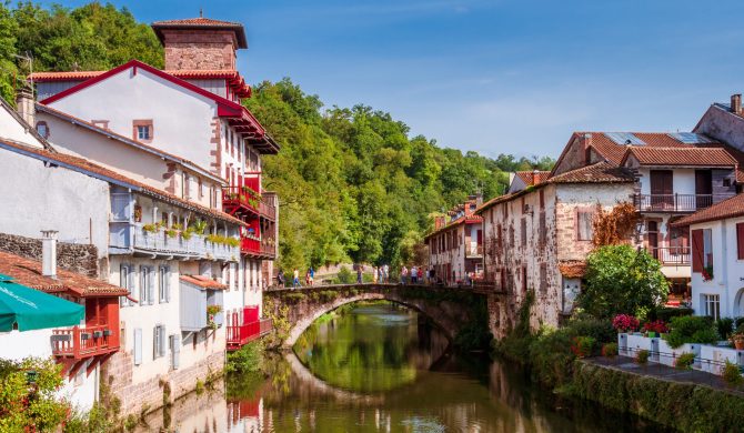 Panoramic view of French white town with red balconies and flowers crossed by a tranquil river. Saint-Jean-Pied-de-Port, France