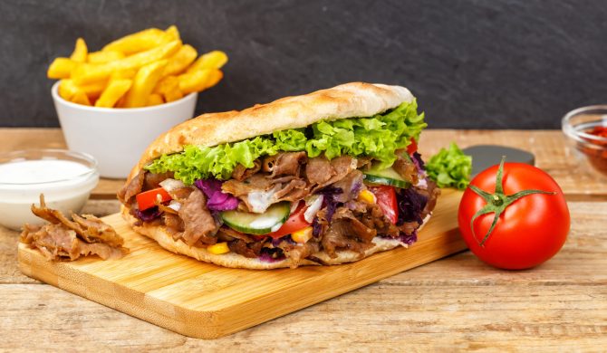 Döner Kebab Doner Kebap fast food meal in flatbread with fries on a wooden board panorama board