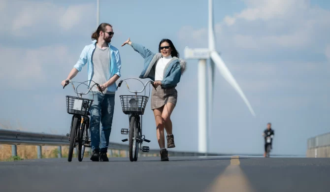 Couple faisant du vélo près d’éoliennes, symbolisant le tourisme durable et les énergies renouvelables