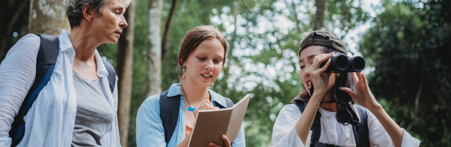 woman family walking in the forest to watching a bird in nature, using binocular for birding by looking on a tree, adventure travel activity in outdoor trekking lifestyle, searching wildlife in jungle