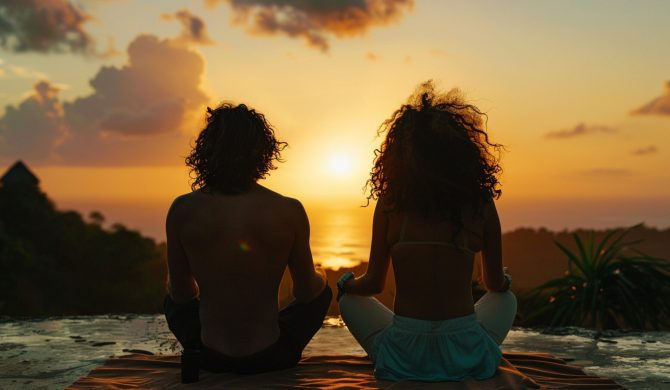 Peaceful couple on beach in the evening in golden hour. Couple meditating at sunset in an exotic location in south east asia. Travelling hippie man and woman on holiday vacation in summer. Wellness.